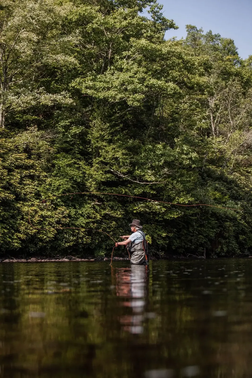 Angler working along a wooded river edge